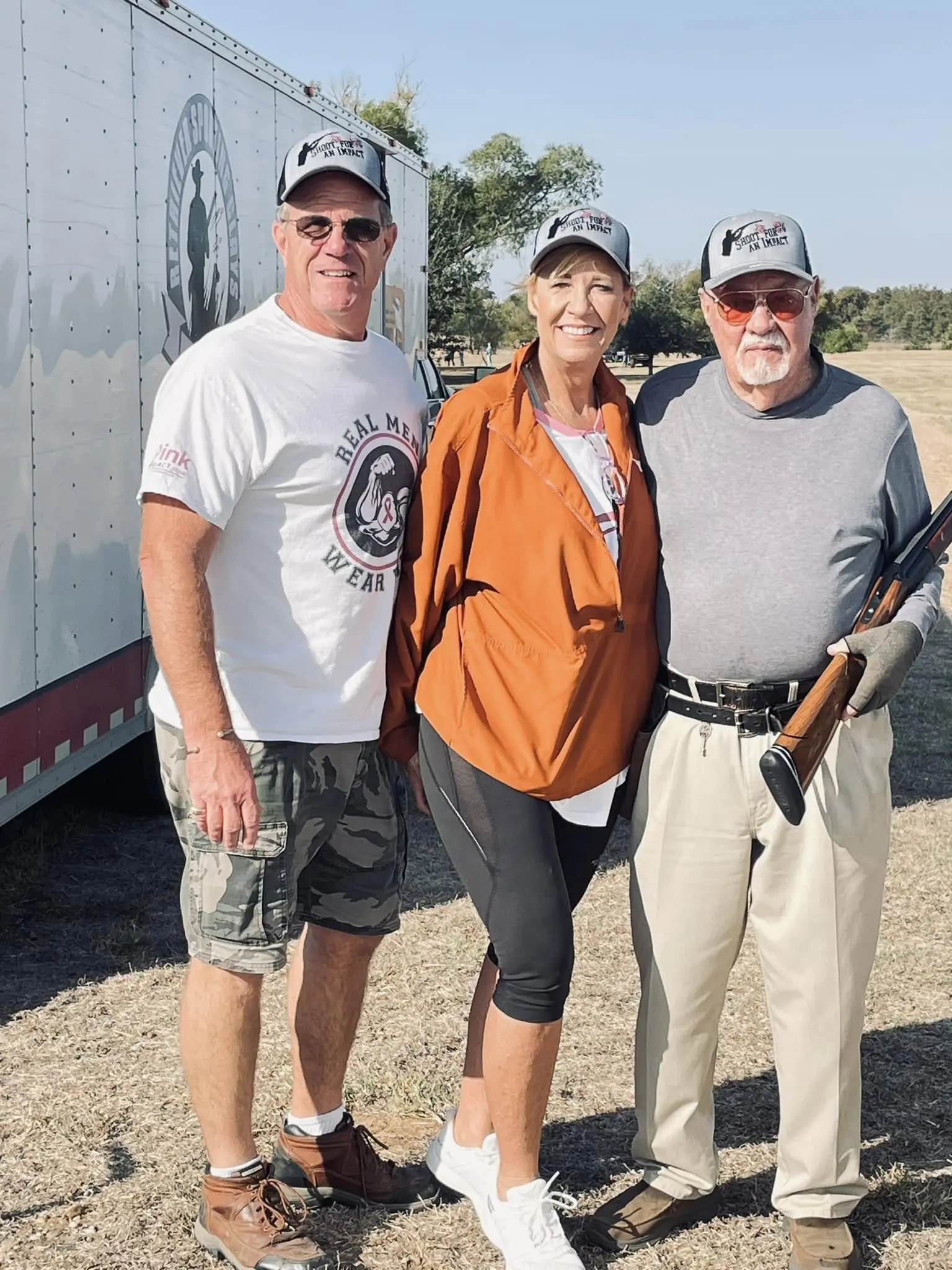 Three people standing next to each other on a dirt field.