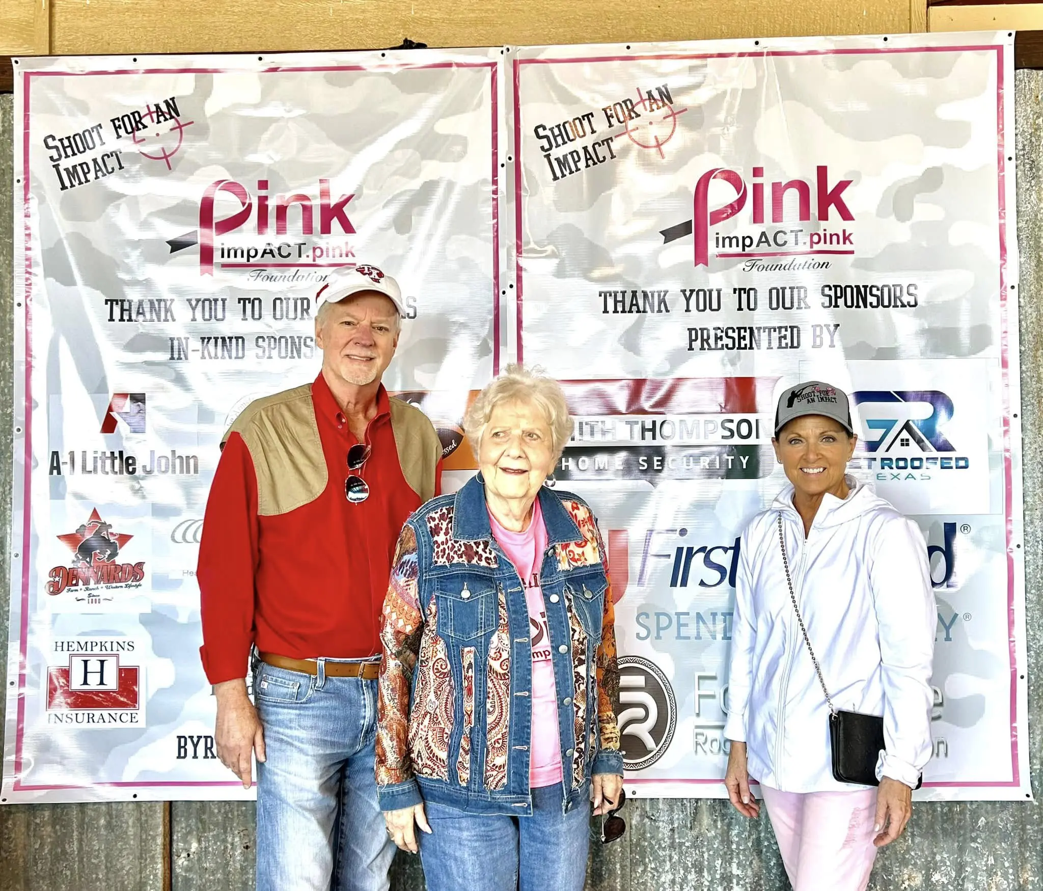 Three people standing in front of a pink sign.