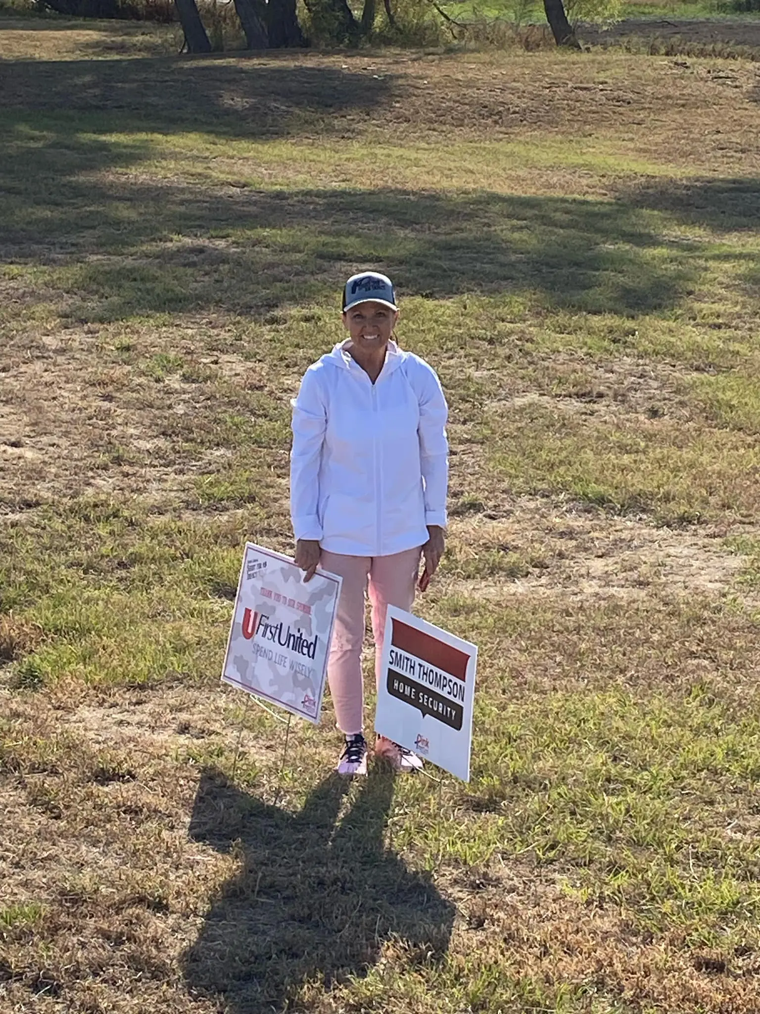 A woman standing in the grass holding two signs.