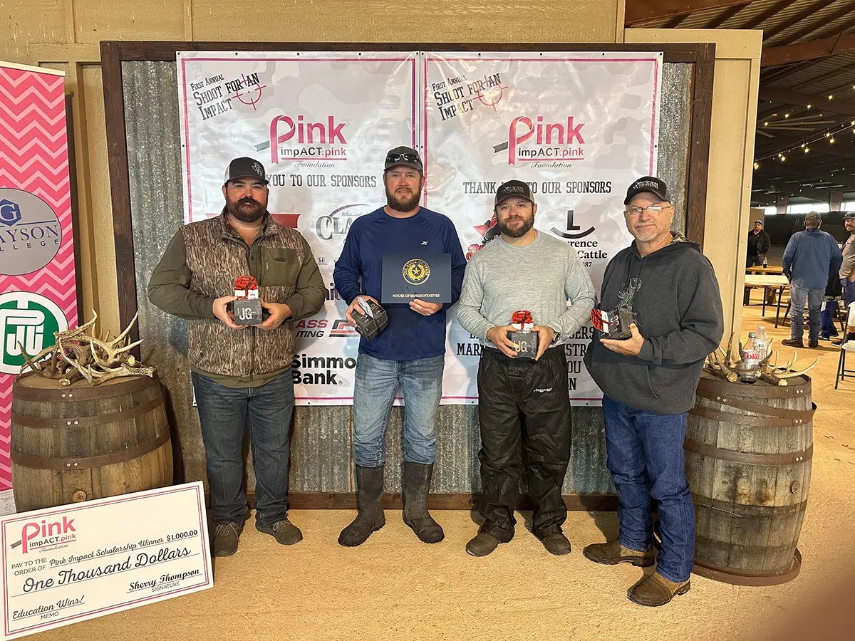 Four men holding up their trophies in front of barrels.